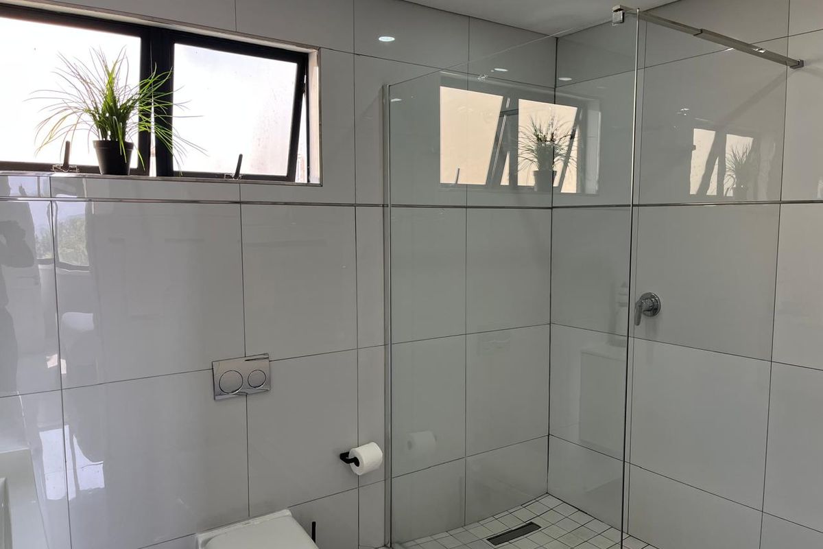 Modern bathroom featuring a glass-enclosed shower, wall-mounted toilet, and sleek white wall tiling with recessed lighting.