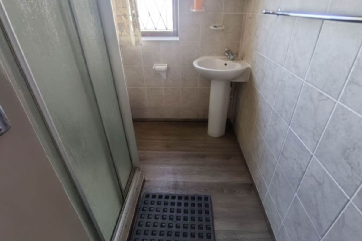 Compact bathroom featuring a pedestal sink, shower enclosure, and tiled walls with wood-look flooring.