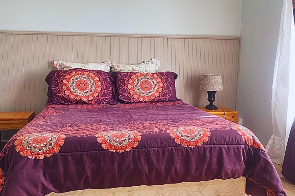 A bedroom featuring a decorative wood-paneled headboard wall and light-toned flooring, providing a neutral base for the space.