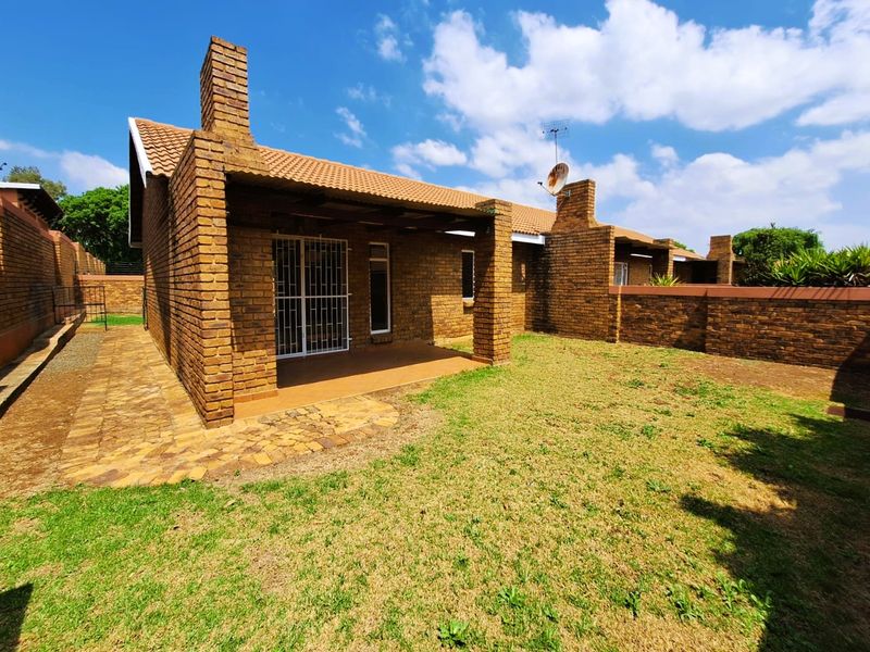 Rear view of a face brick townhouse featuring a covered patio, paved walkway, and a private garden area with boundary walls.