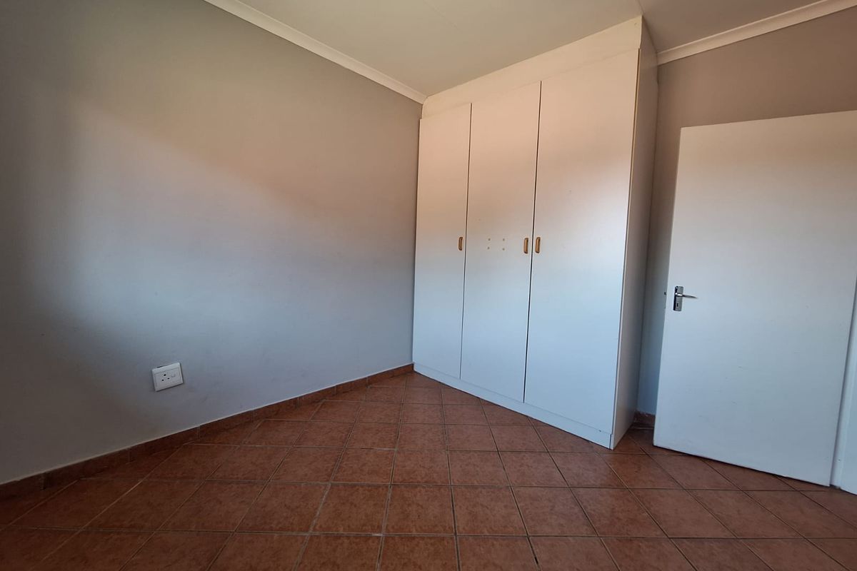 An empty bedroom featuring tiled flooring, neutral wall paint, and a built-in white wardrobe.
