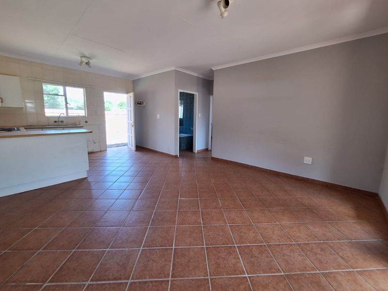 Spacious open-plan living area featuring tiled flooring, a functional kitchen with built-in cabinetry, and direct access to the exterior.