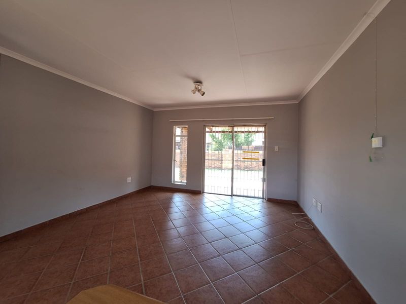 A spacious, empty living room featuring neutral walls, tiled flooring, and a sliding glass door with a security gate leading to the exterior.