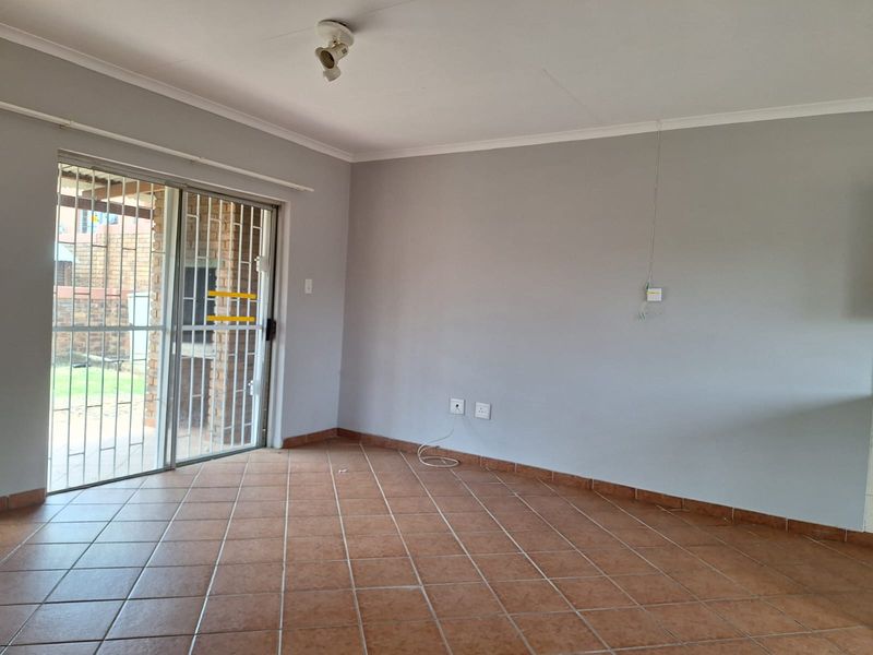 An empty living room featuring tiled flooring, neutral walls, and a sliding glass door with a security gate leading to the outdoor area.