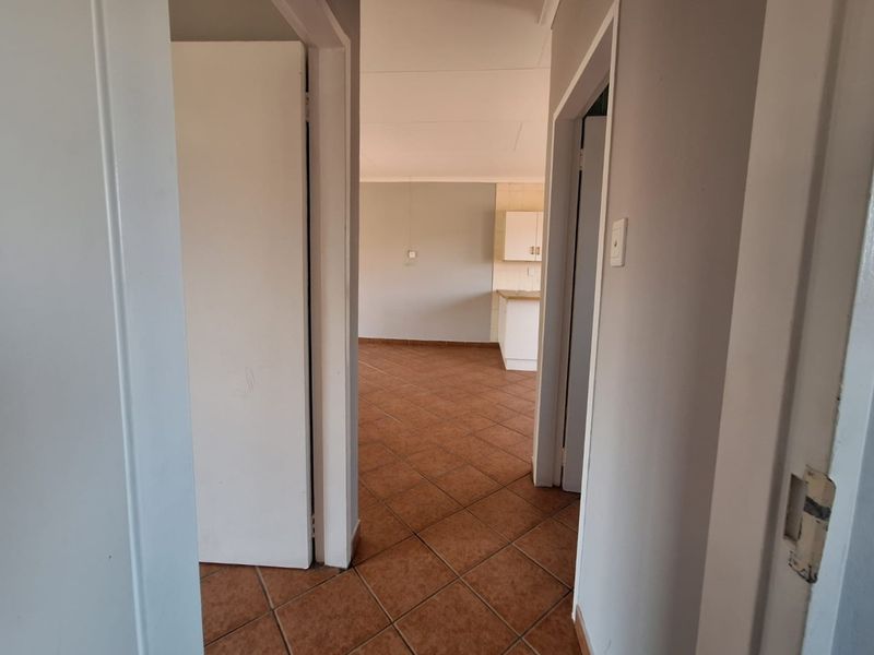 A view from the hallway looking into an open-plan living and kitchen area featuring tiled flooring and neutral wall finishes.