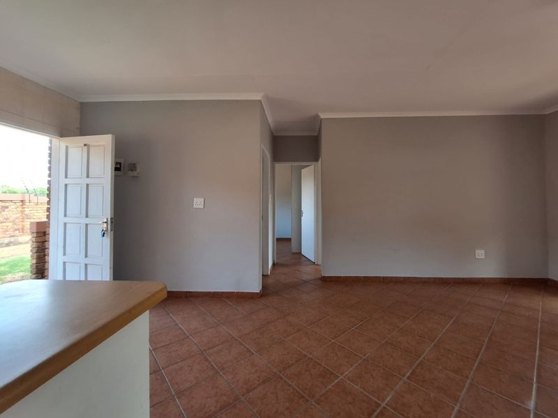 An empty living area featuring terracotta floor tiles, neutral grey walls, and direct access to the exterior through a panelled door.