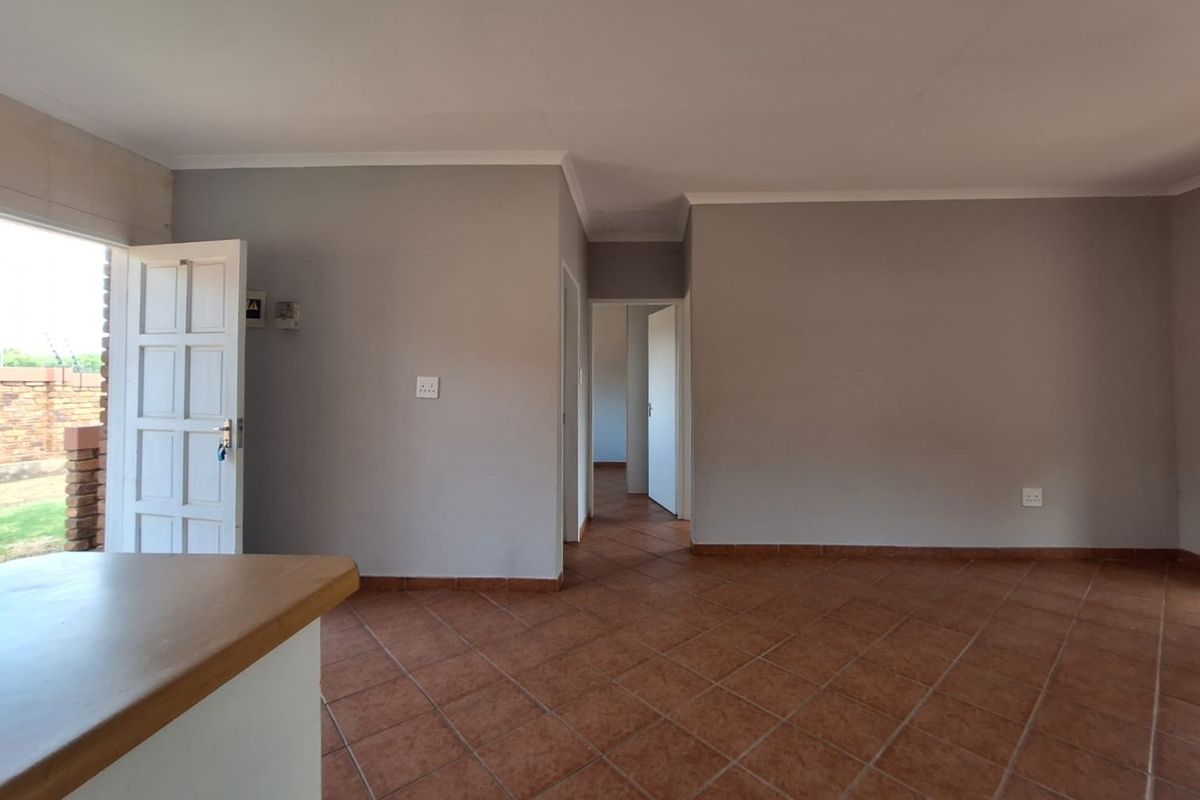 An empty living area featuring terracotta floor tiles, neutral grey walls, and direct access to the exterior through a panelled door.