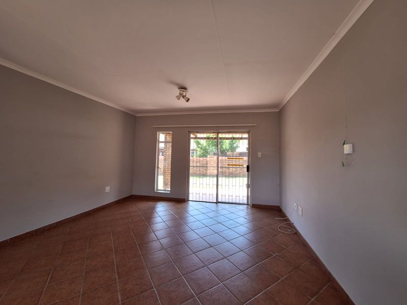 A spacious, empty living room featuring neutral walls, tiled flooring, and a sliding glass door with a security gate leading to the backyard.