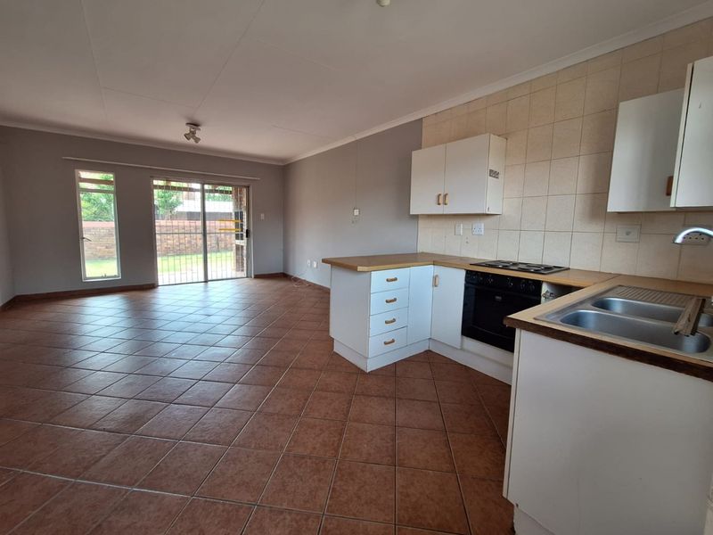 Spacious open-plan living area featuring a functional kitchen with built-in oven, hob, and tiled flooring, leading directly to an outdoor patio area.