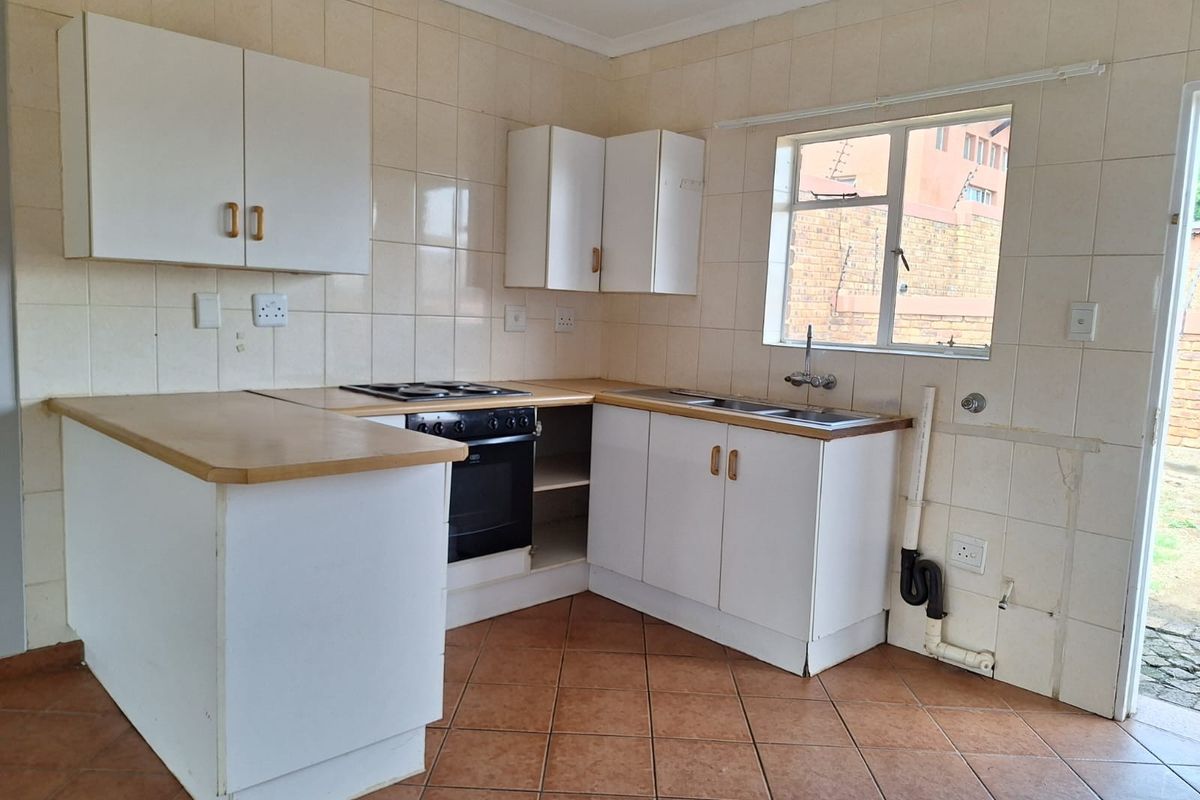 A functional kitchen featuring white cabinetry, laminate countertops, built-in oven and hob, and tiled finishes, ready for a modern update.