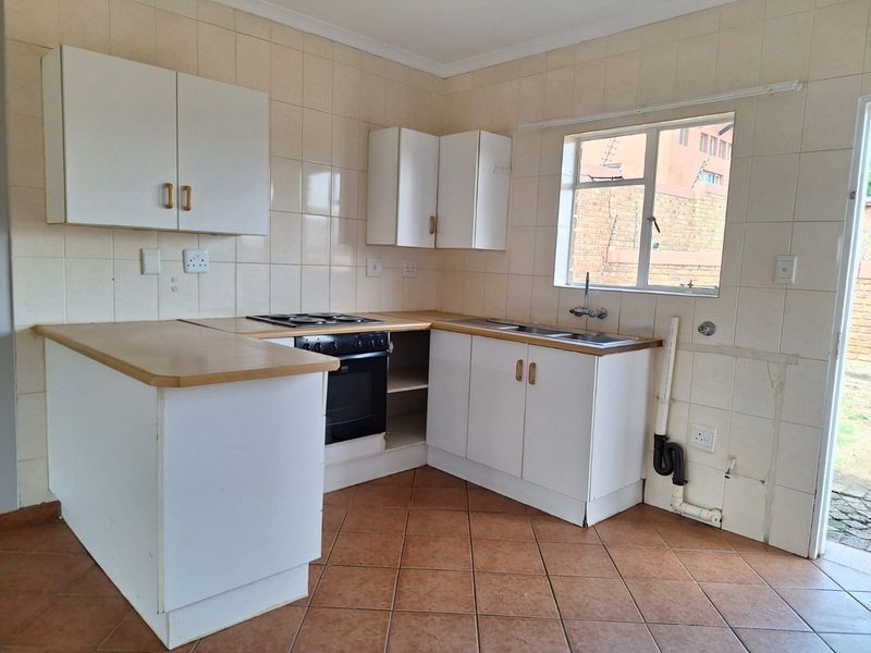 A functional kitchen featuring white cabinetry, laminate countertops, built-in oven and hob, and tiled finishes, ready for a modern update.