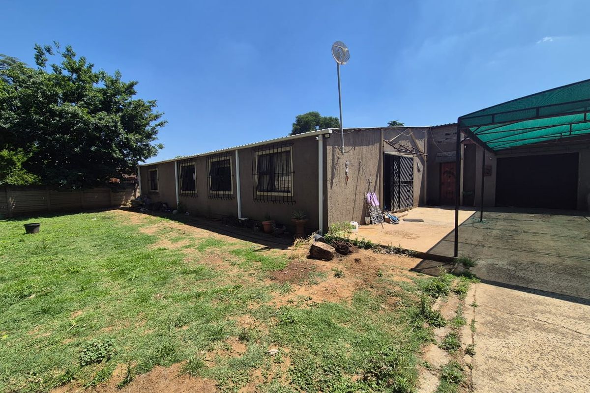 Rear view of the property featuring a lawn, covered patio area, concrete driveway, and security bars on the windows.