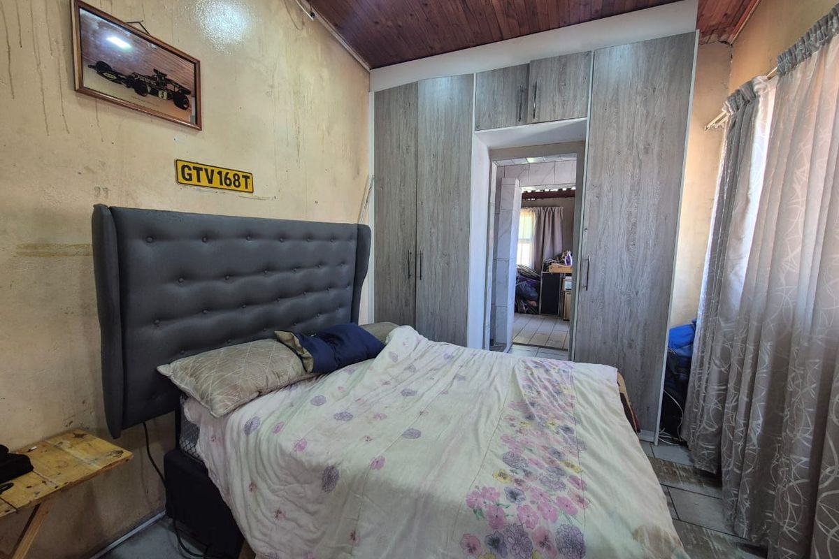 A bedroom featuring built-in cupboards, a timber ceiling, and tiled flooring, requiring cosmetic updates to the wall finishes.