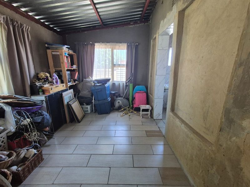 A living area featuring tiled floors and an exposed metal ceiling, currently requiring finishing work on the walls and ceiling structure.