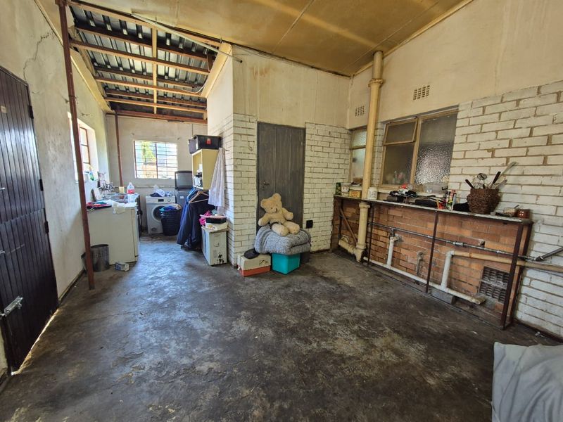 A utility or laundry space featuring exposed brickwork, concrete flooring, and exposed roof rafters, offering significant potential for renovation and functional improvement.