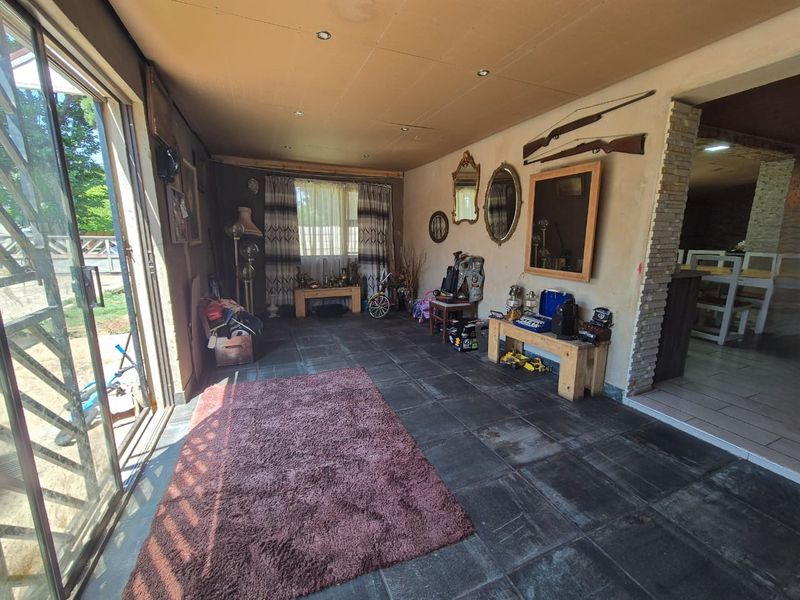 A covered patio area featuring dark tiled flooring, recessed lighting, and sliding glass doors leading to the garden, with a stone-clad accent wall.