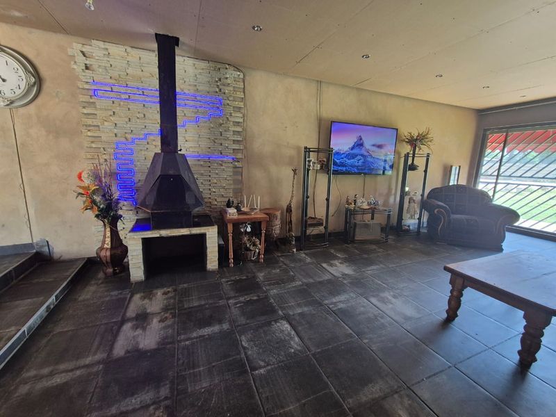 Spacious living room featuring a stone-clad feature wall with a freestanding fireplace, dark tiled flooring, and direct access to the outdoor area.
