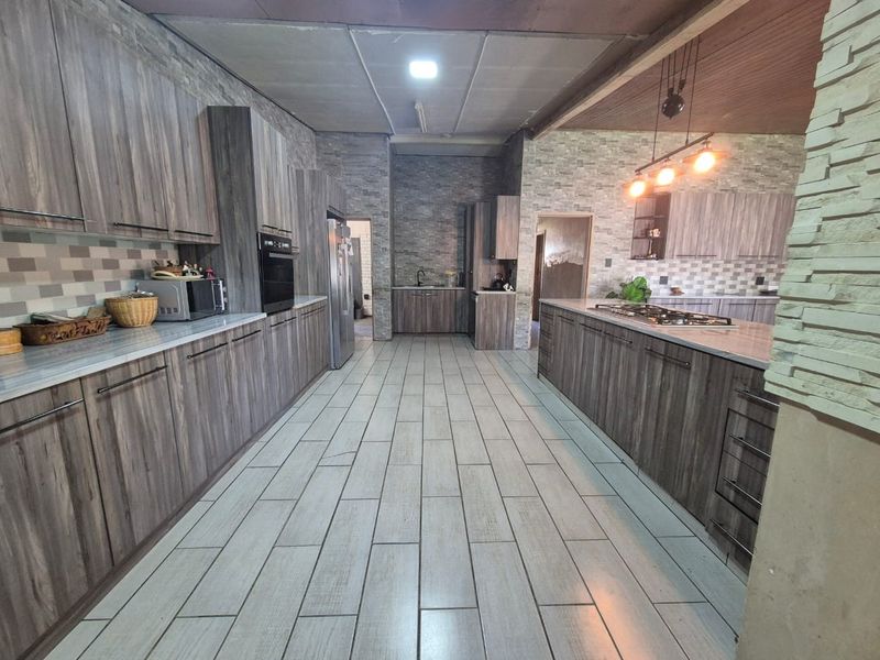 Spacious modern kitchen featuring extensive wood-grain cabinetry, stone countertops, a central island with a gas hob, and contemporary tiled flooring.