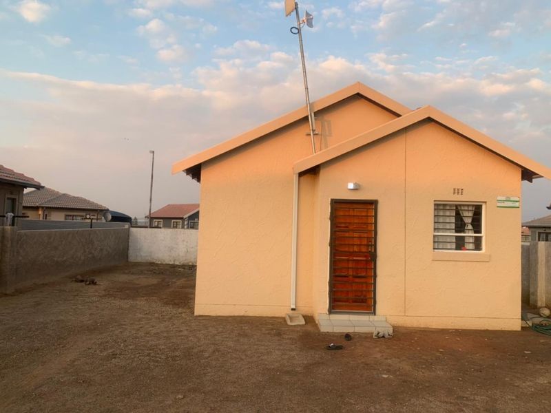 Rear view of the property featuring a secure entrance door, window with burglar bars, and a surrounding boundary wall.