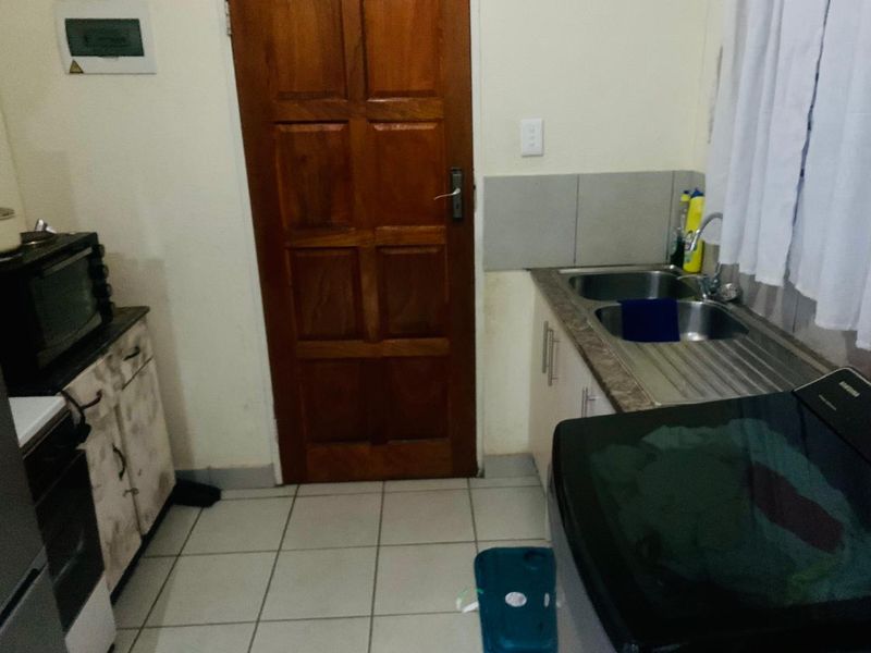 A functional laundry area featuring tiled flooring, built-in cabinetry, a double stainless steel sink, and direct access via a timber door.