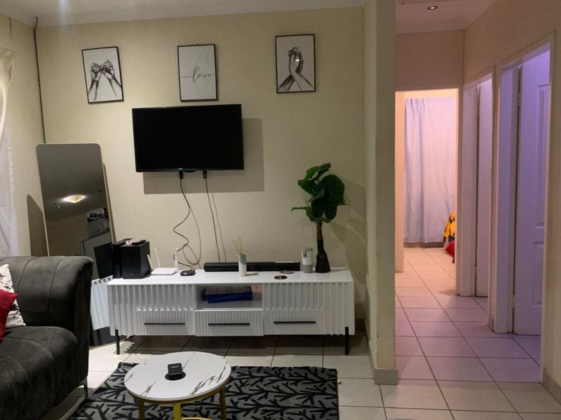 A living room area featuring tiled flooring and recessed ceiling lighting, with a clear view into the adjacent hallway.