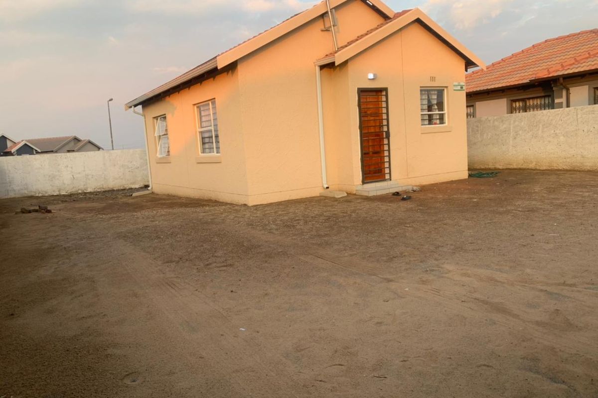 A detached single-story house featuring a tiled roof, security gate, and an expansive, unlandscaped yard enclosed by a perimeter wall.
