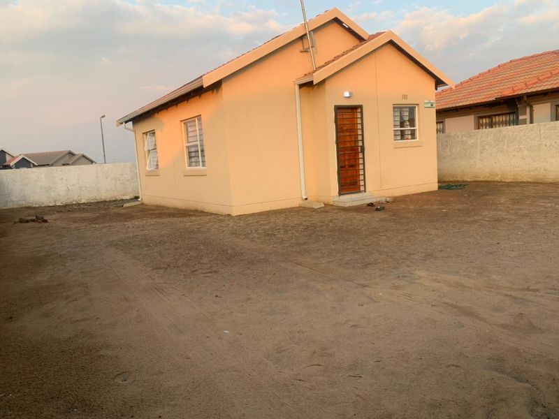 A detached single-story house featuring a tiled roof, security gate, and an expansive, unlandscaped yard enclosed by a perimeter wall.