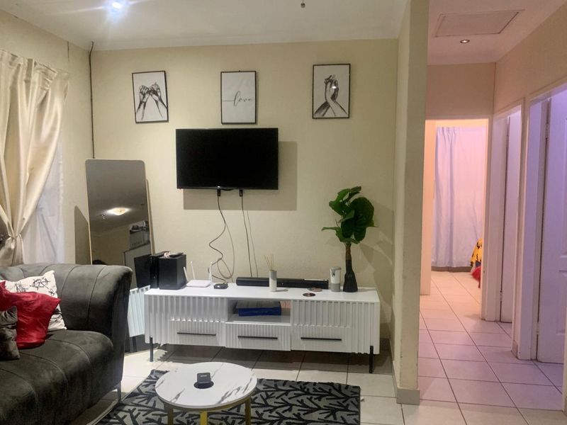 A living room area featuring tiled flooring and recessed ceiling lighting, with an adjacent hallway leading to other parts of the home.