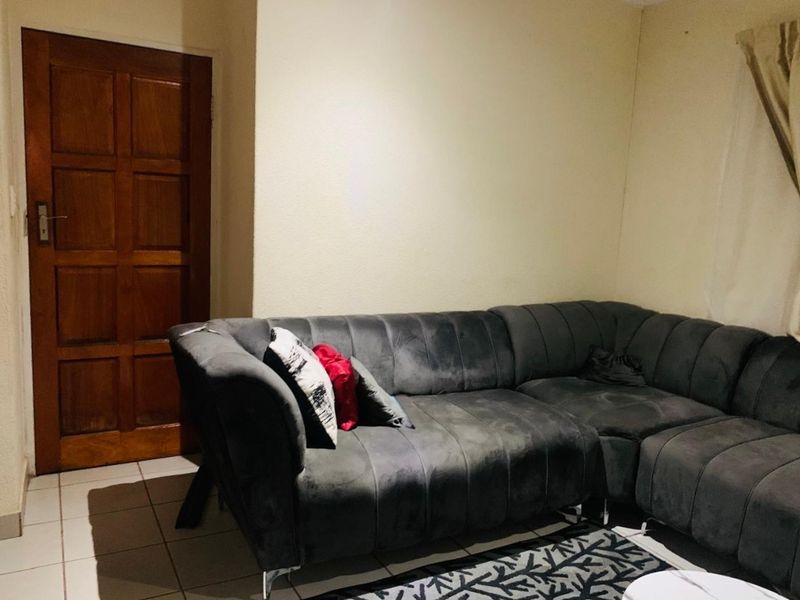 A living room area featuring tiled flooring and a traditional wooden door, providing a functional space for relaxation.