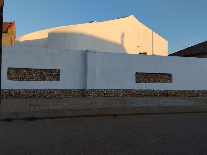 A street-facing view of a property featuring a white plastered boundary wall with decorative stone-clad inserts and a paved sidewalk.