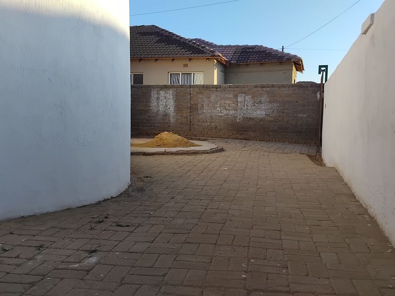 A rear exterior area featuring paved flooring and a boundary wall, offering a functional outdoor space with potential for landscaping improvements.