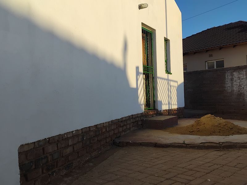 Rear exterior view of the property featuring a paved courtyard, security gate, and boundary wall with ongoing maintenance visible.