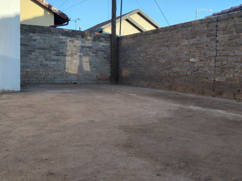 A rear outdoor area featuring an exposed brick boundary wall and a concrete slab base, offering potential for landscaping or patio development.