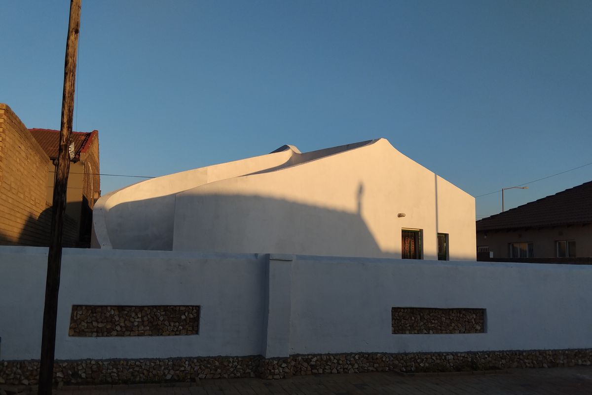 Front view of a residential property featuring a white boundary wall with stone inlay and a distinctive curved roofline design.