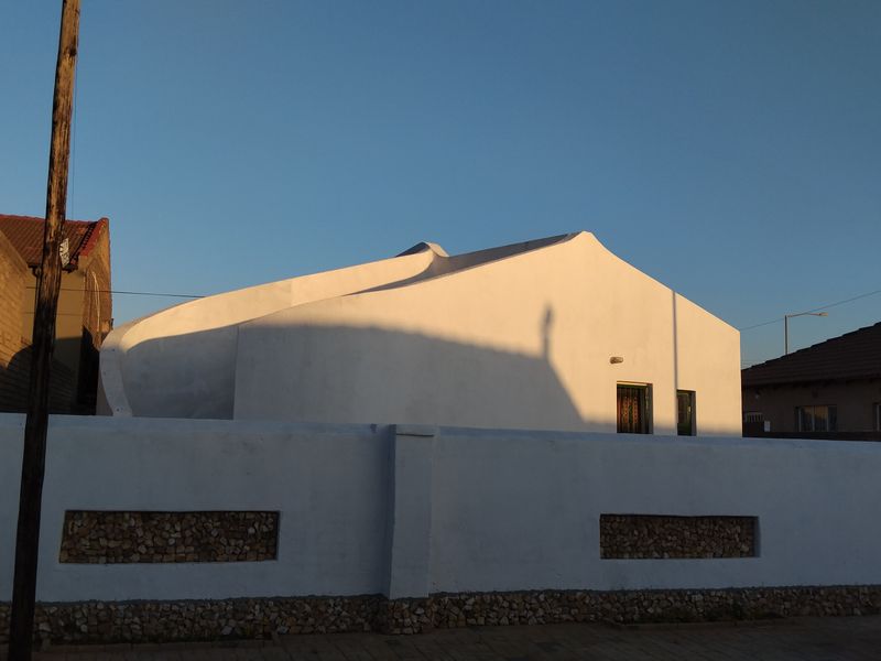 Front view of a residential property featuring a white boundary wall with stone inlay and a distinctive curved roofline design.