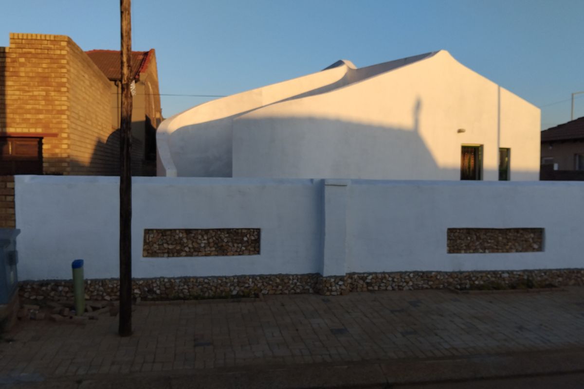 Front view of a modern house featuring a distinctive curved roofline and a white boundary wall with decorative stone inlay.
