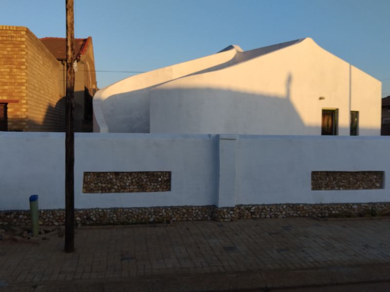 Front view of a modern house featuring a distinctive curved roofline and a white boundary wall with decorative stone inlay.