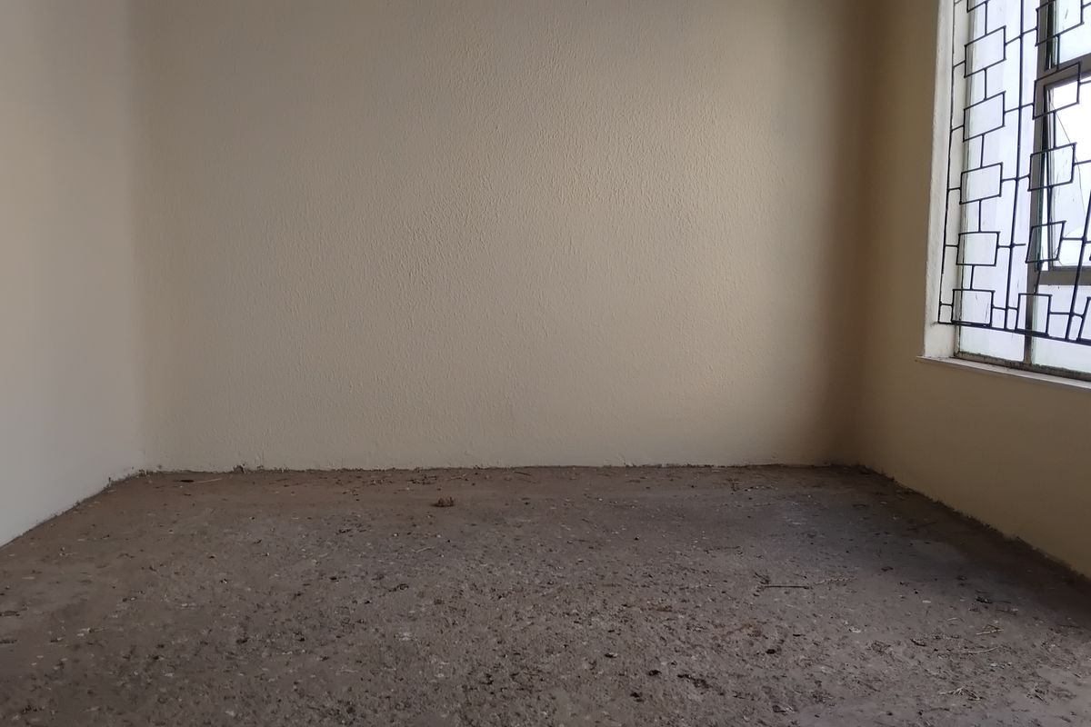 An empty bedroom featuring plain walls, a window with security bars, and an unfinished concrete floor surface.