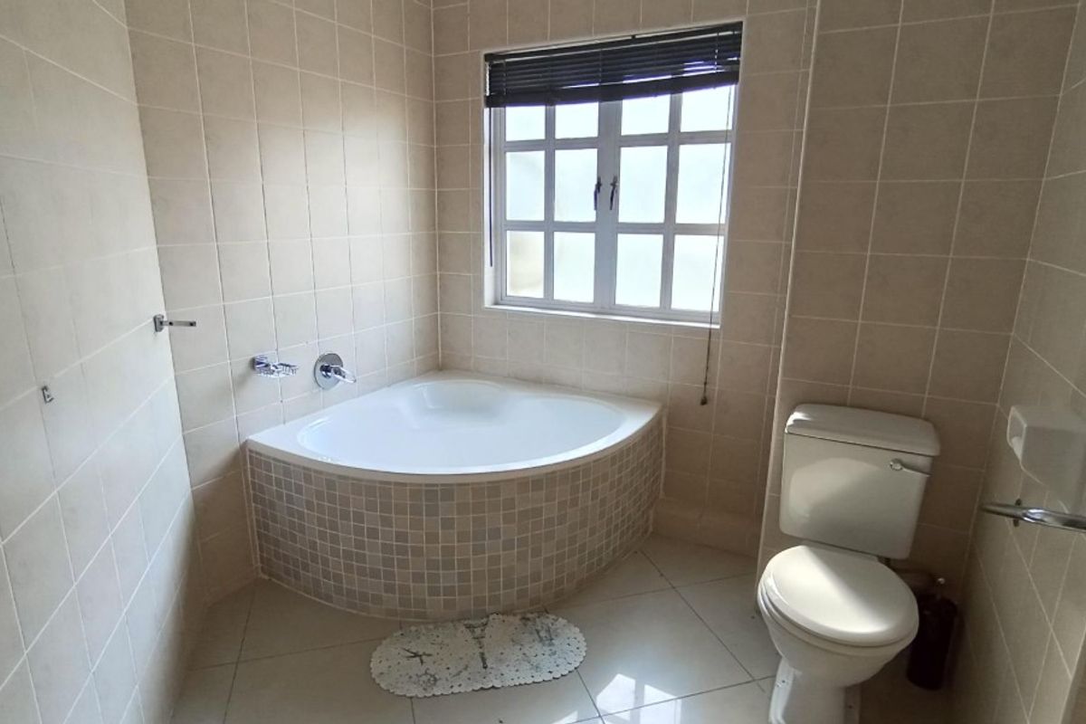 A functional bathroom featuring a corner bathtub with mosaic tiling, a standard toilet, and neutral wall tiles.