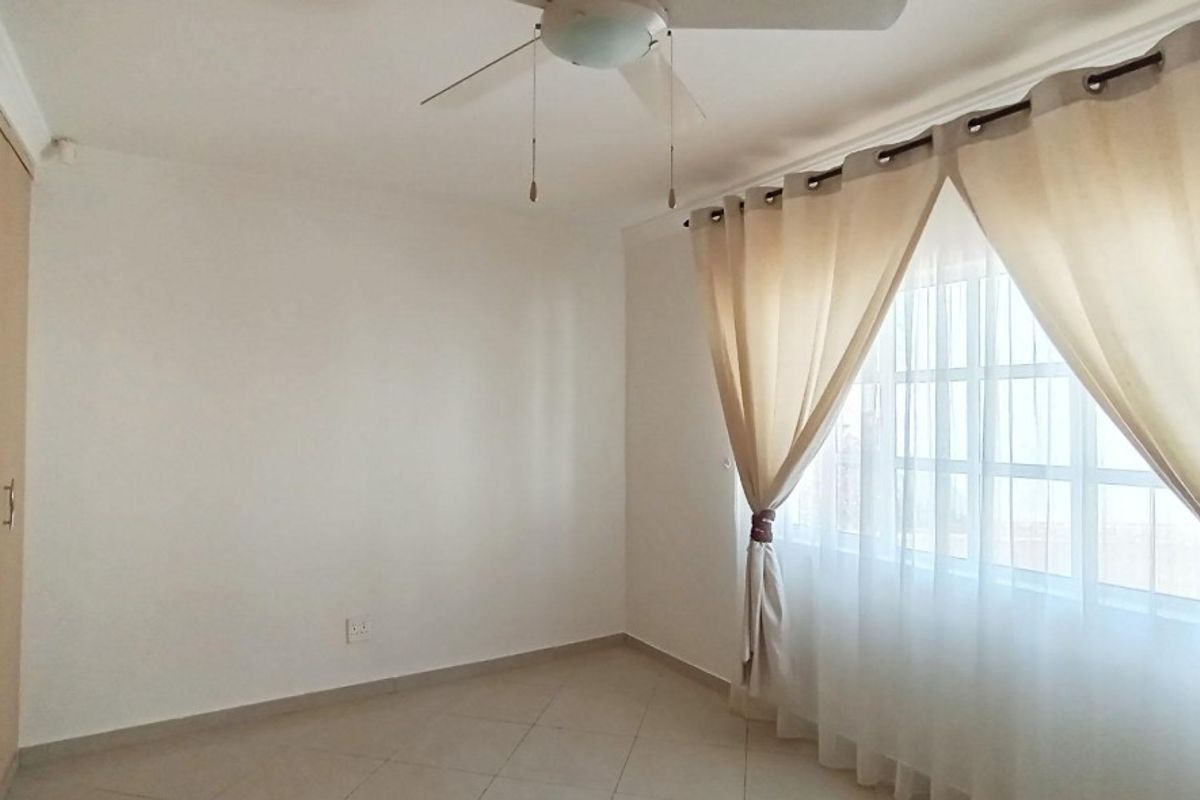 A bright bedroom featuring built-in cupboards, tiled flooring, and a ceiling fan, offering a clean and functional living space.