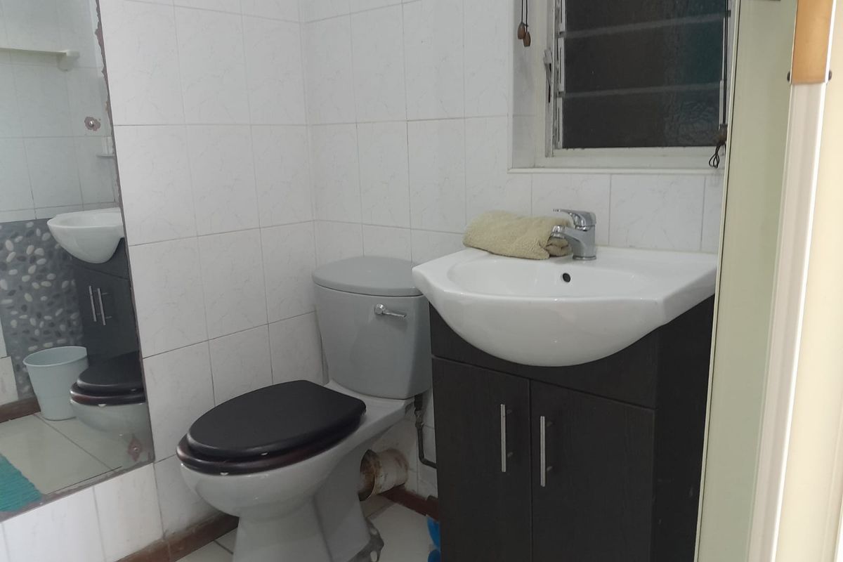 A functional bathroom featuring a vanity cabinet with a basin, a toilet, and wall-mounted mirror, finished with white wall tiles.