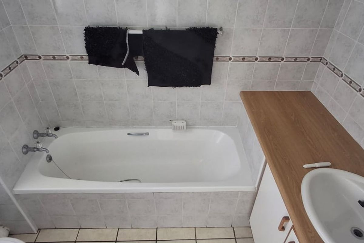 A functional bathroom featuring a built-in bathtub with chrome fixtures and a vanity unit with a countertop basin.
