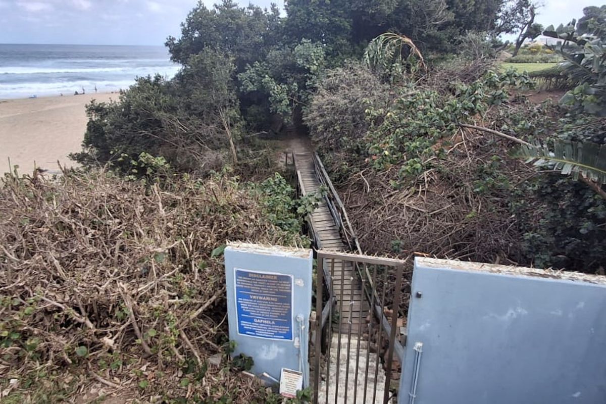 A private beach access path featuring a wooden walkway and metal gate, leading directly to the coastline with ocean views.