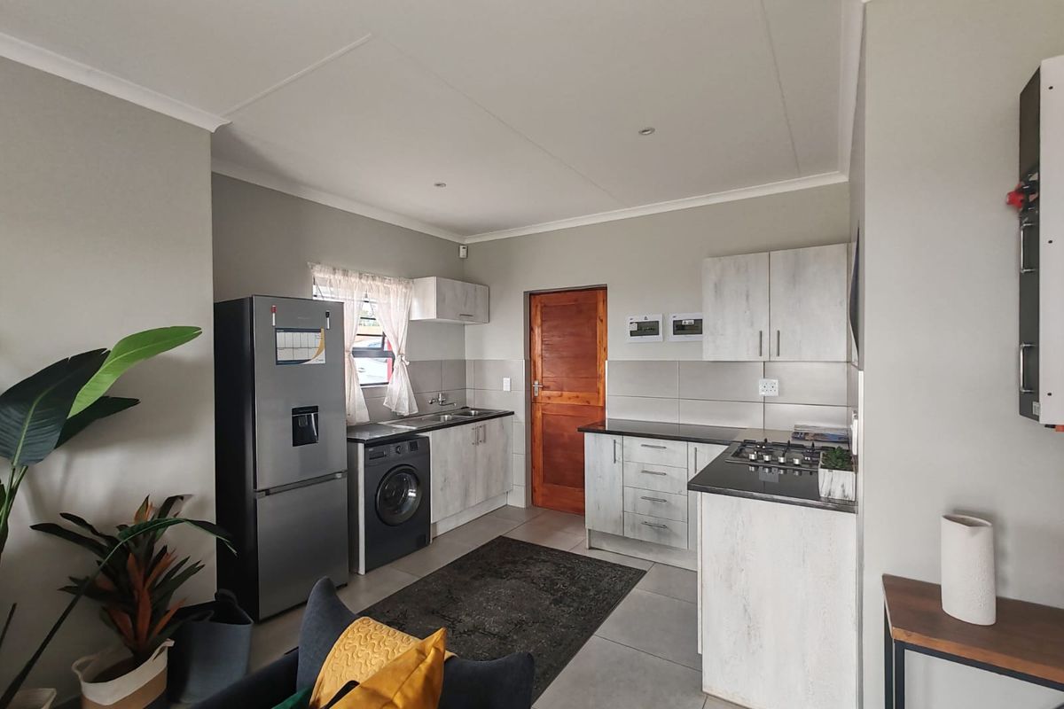 A functional kitchen featuring light wood-grain cabinetry, dark countertops, a built-in gas hob, and integrated laundry plumbing.