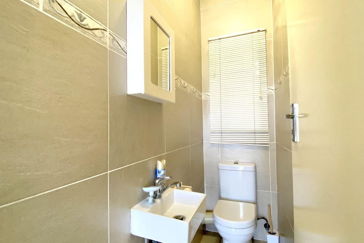 A compact guest bathroom featuring floor-to-ceiling wall tiles, a wall-mounted basin, and a standard toilet.