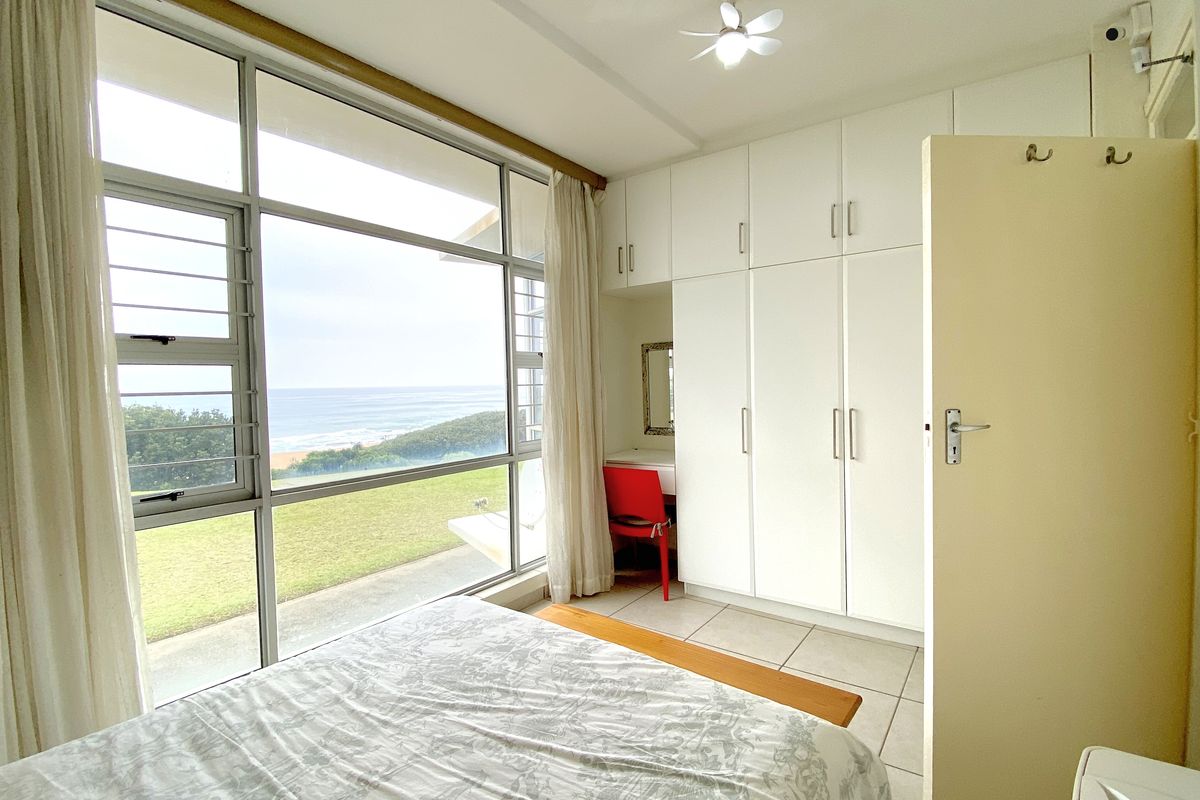 Bright bedroom featuring floor-to-ceiling windows with ocean views, built-in white cabinetry, and tiled flooring.