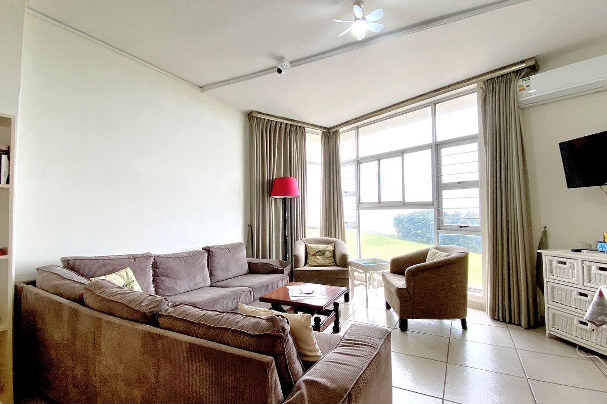 A bright living room featuring large windows with natural light, tiled flooring, and a wall-mounted air conditioning unit.