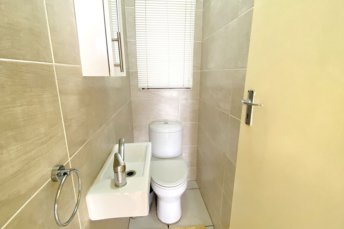 A compact guest bathroom featuring floor-to-ceiling neutral wall tiles, a wall-mounted basin, and a modern toilet.