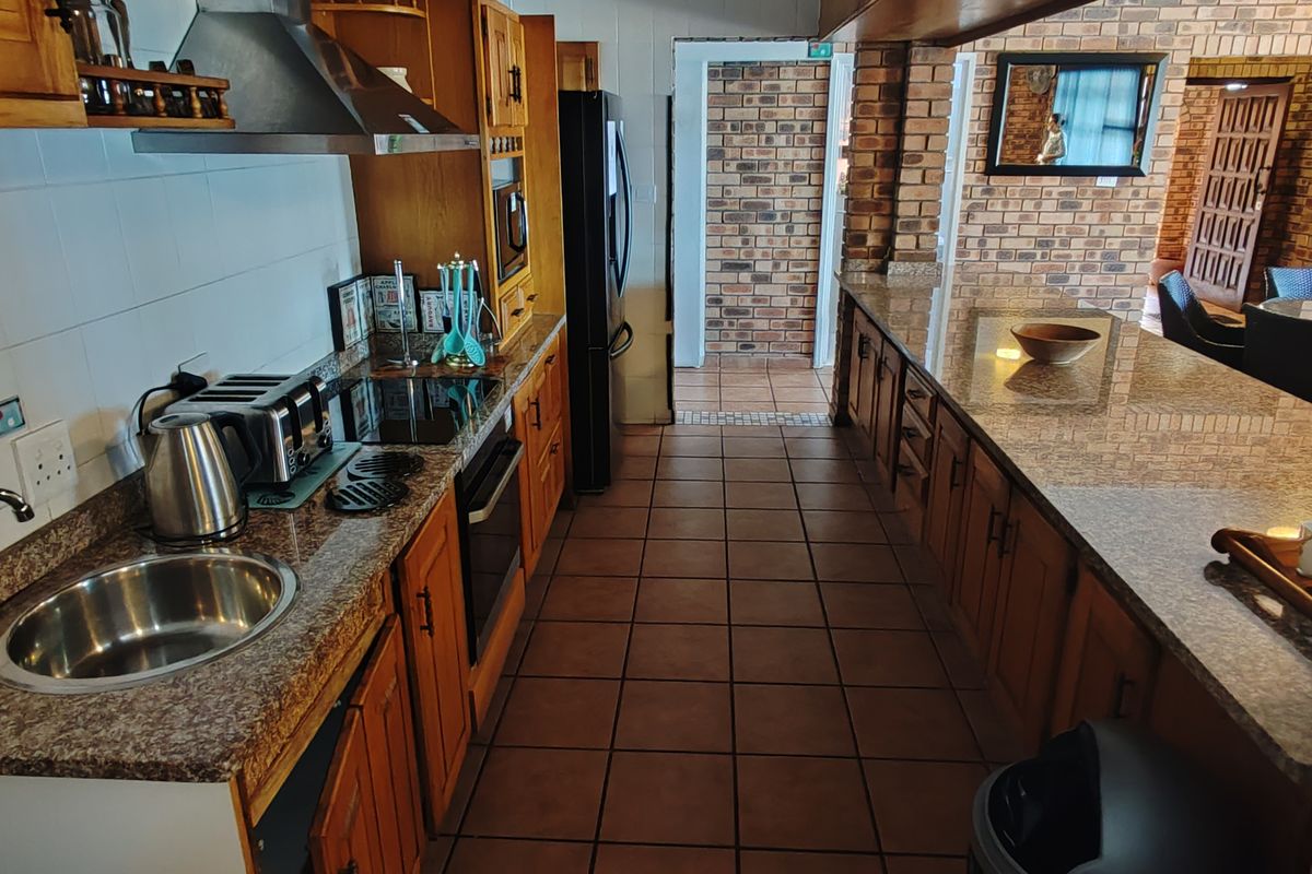 Spacious kitchen featuring granite countertops, wooden cabinetry, a built-in oven, extractor fan, and a breakfast bar, with tiled flooring throughout.