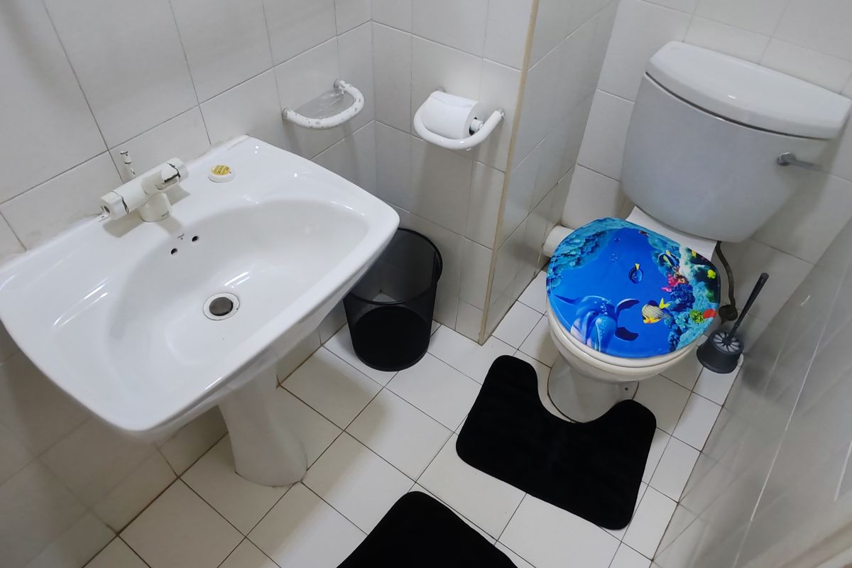 A compact bathroom featuring a pedestal sink, a standard toilet, and fully tiled walls and flooring.